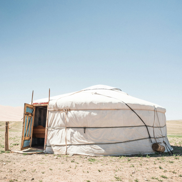 Photo of a white ger in Mongolia, sand around and blue sky in the background